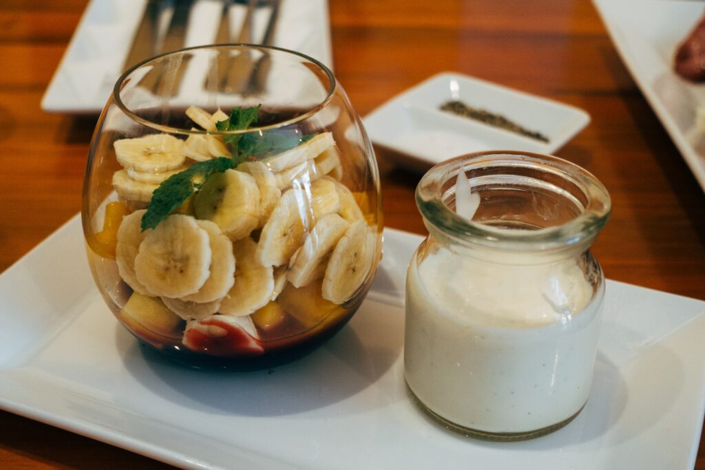 Čaša jogurta pored zdjele izrezanih banana.
